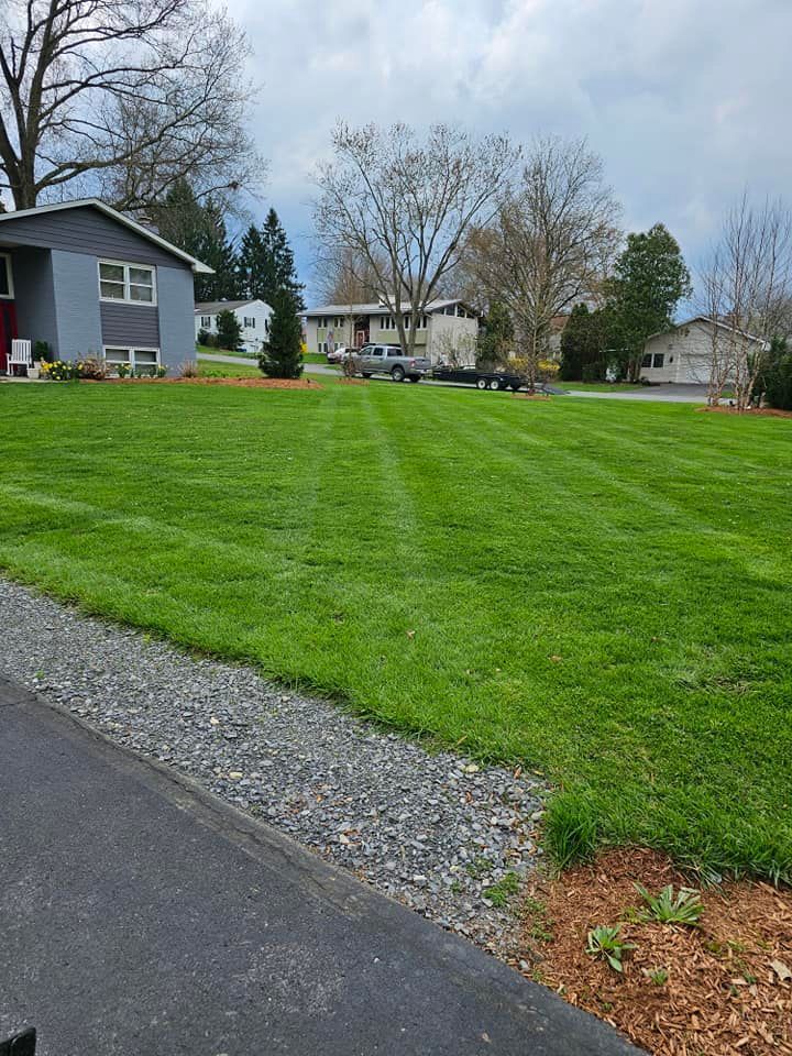 A view of a neatly mown green lawn in front of houses under a cloudy sky.
