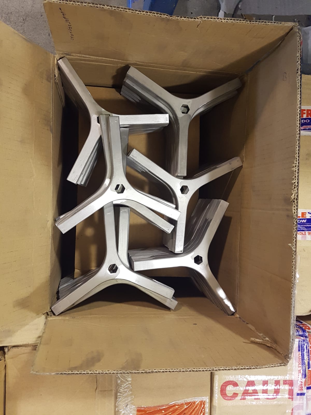 Scatola di cartone piena di staffe a X in metallo argentato impilate una sull'altra.