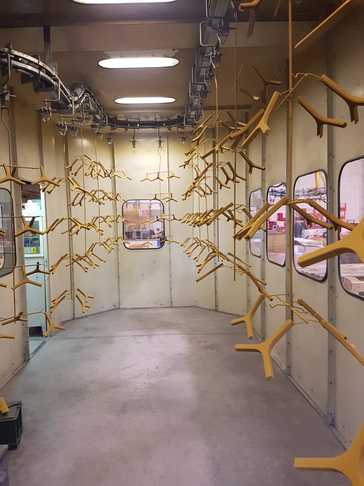 Stretta stanza interna con trespoli di legno giallo e rami che rivestono le pareti, illuminata da luci fluorescenti.