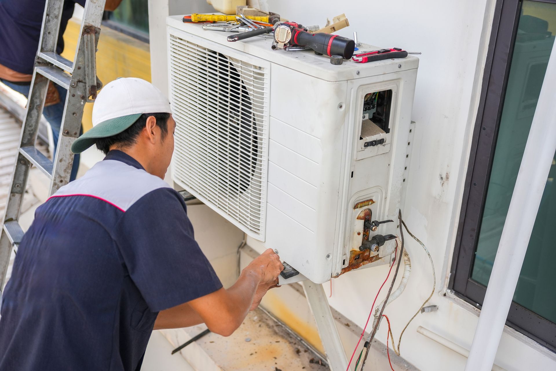A man is fixing an air conditioner on the side of a building.