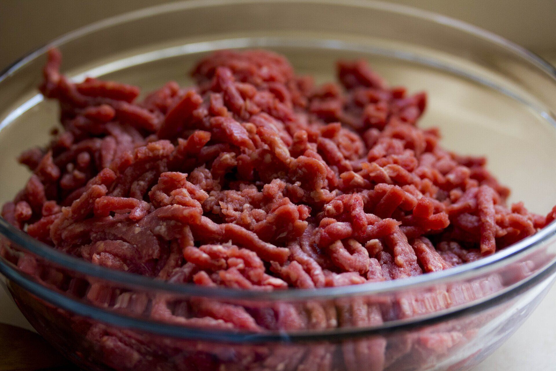 Raw ground beef in a clear glass bowl, close-up view.