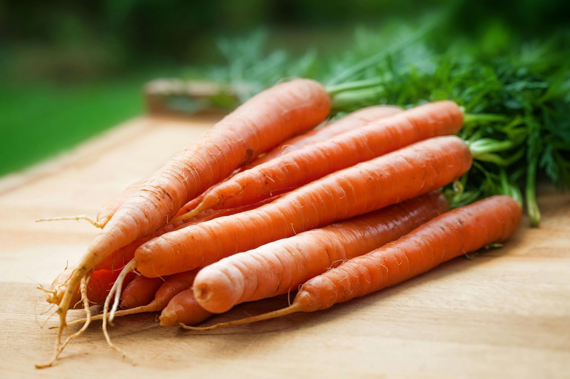 Pile of orange carrots with green leafy tops on a wooden cutting board.