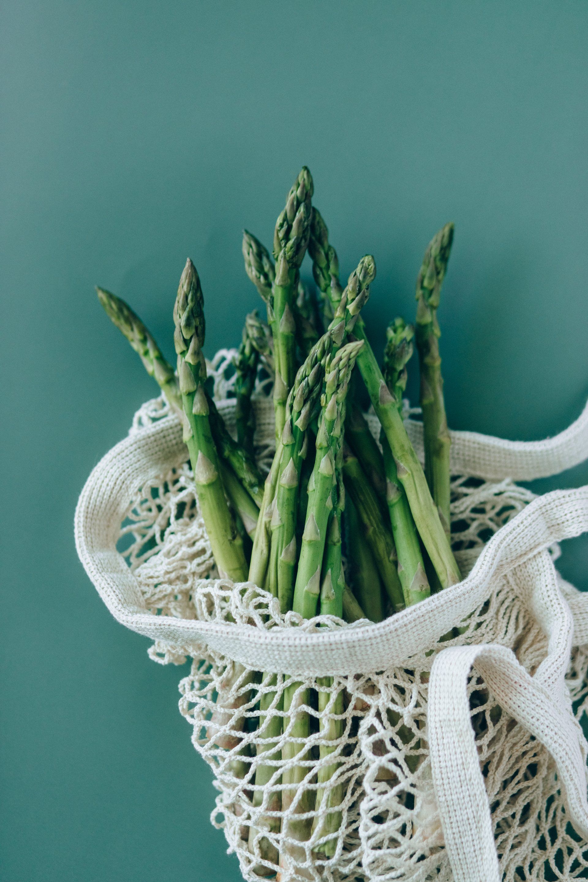 Asparagus spears in a mesh bag, against a teal background.