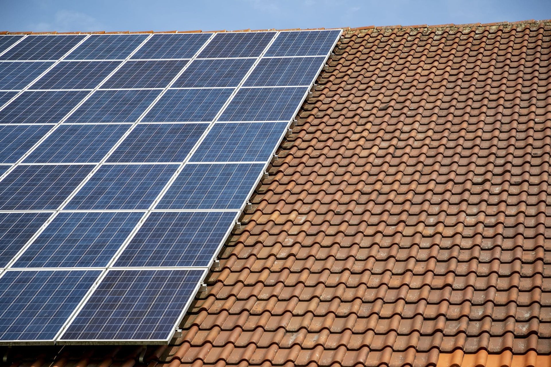 A row of solar panels on top of a tiled roof.