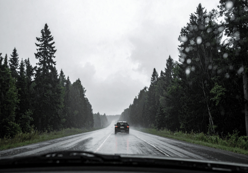 Car driving on a wet forest highway in heavy rain with water droplets on the windshield.