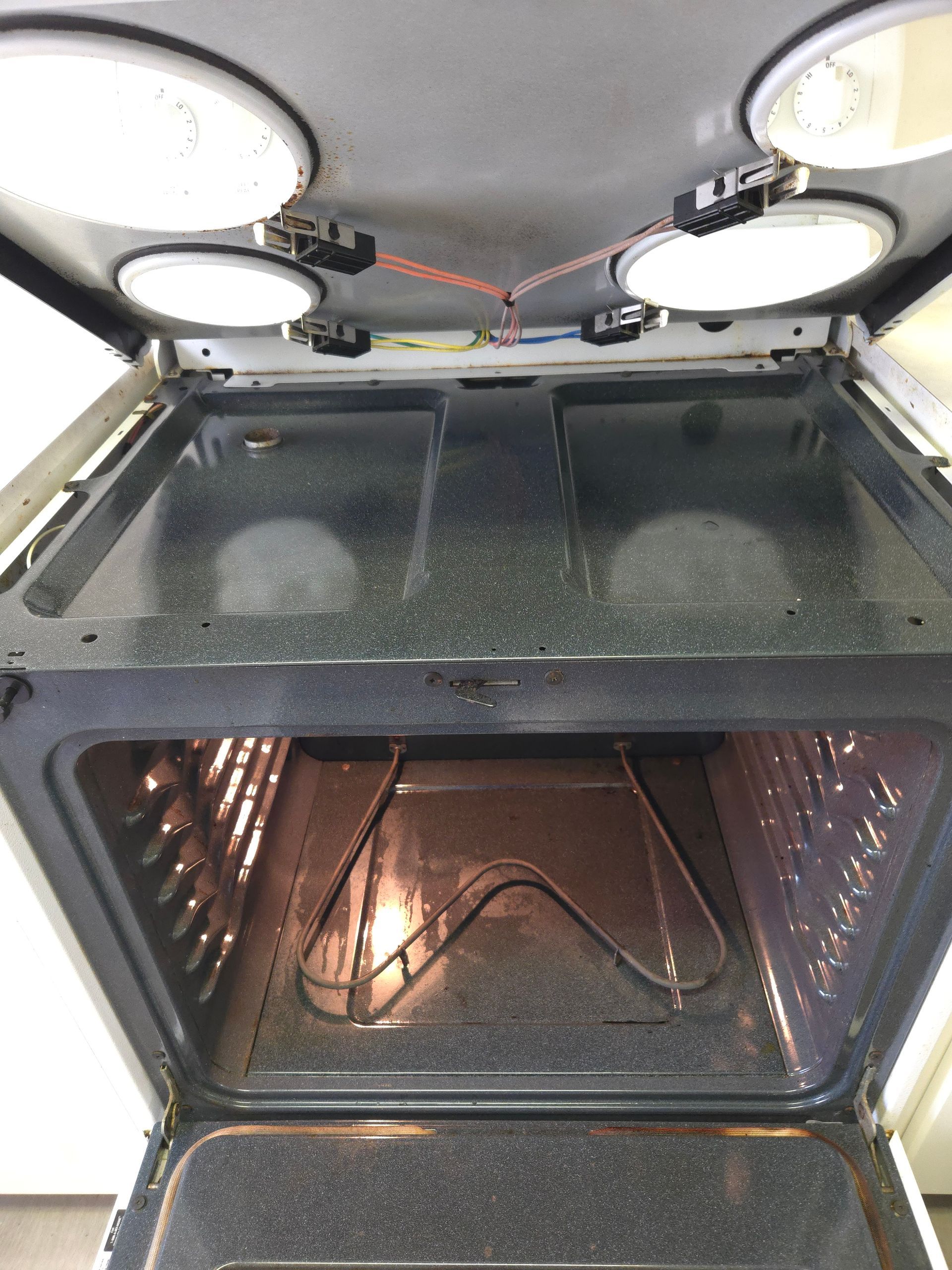 Inside of a white oven with the door open, showing the cooktop, interior of the oven, and heating elements.