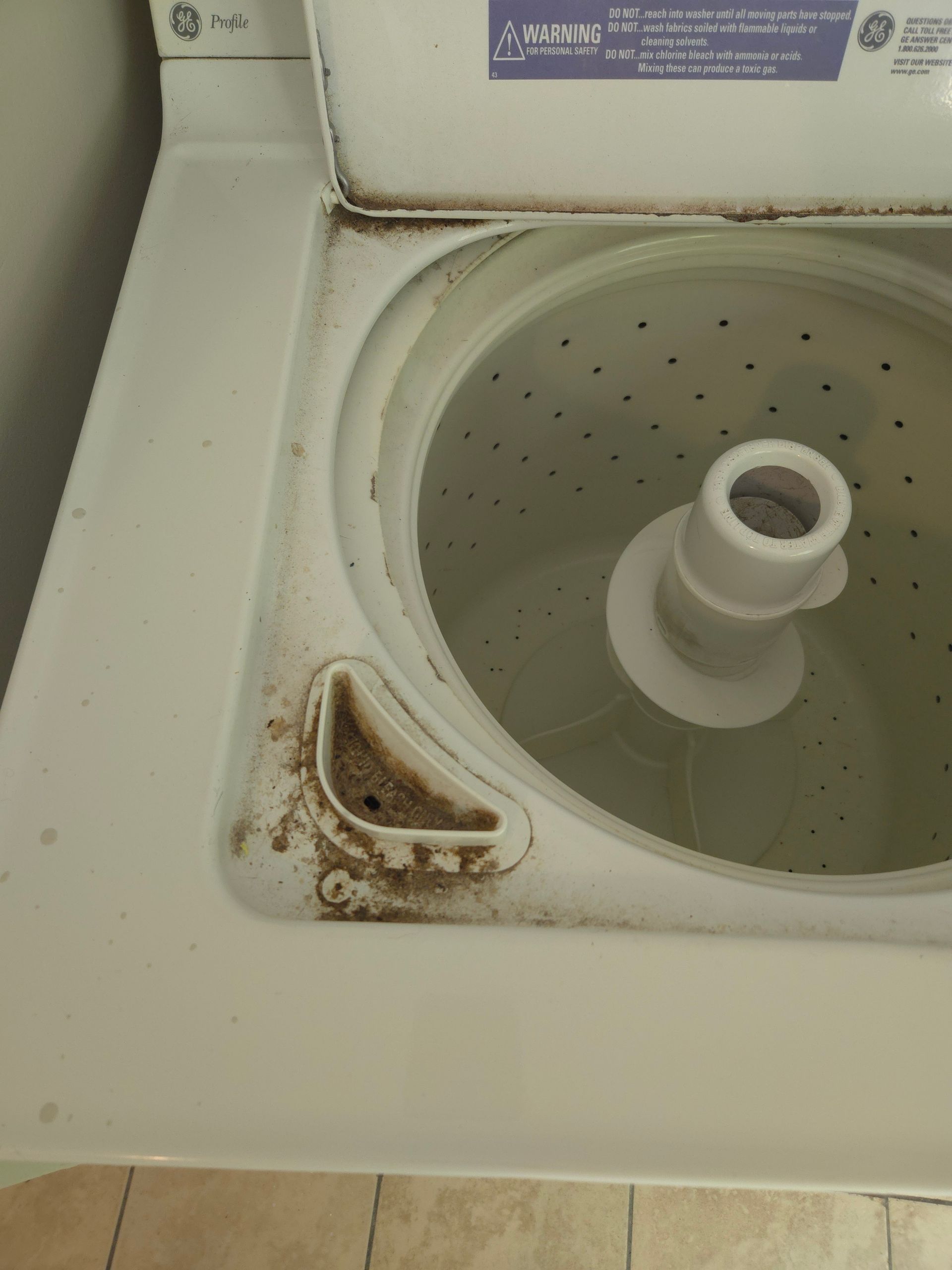 A dirty top-loading washing machine with mold and mildew around the rim and detergent dispenser. The interior tub is visible.