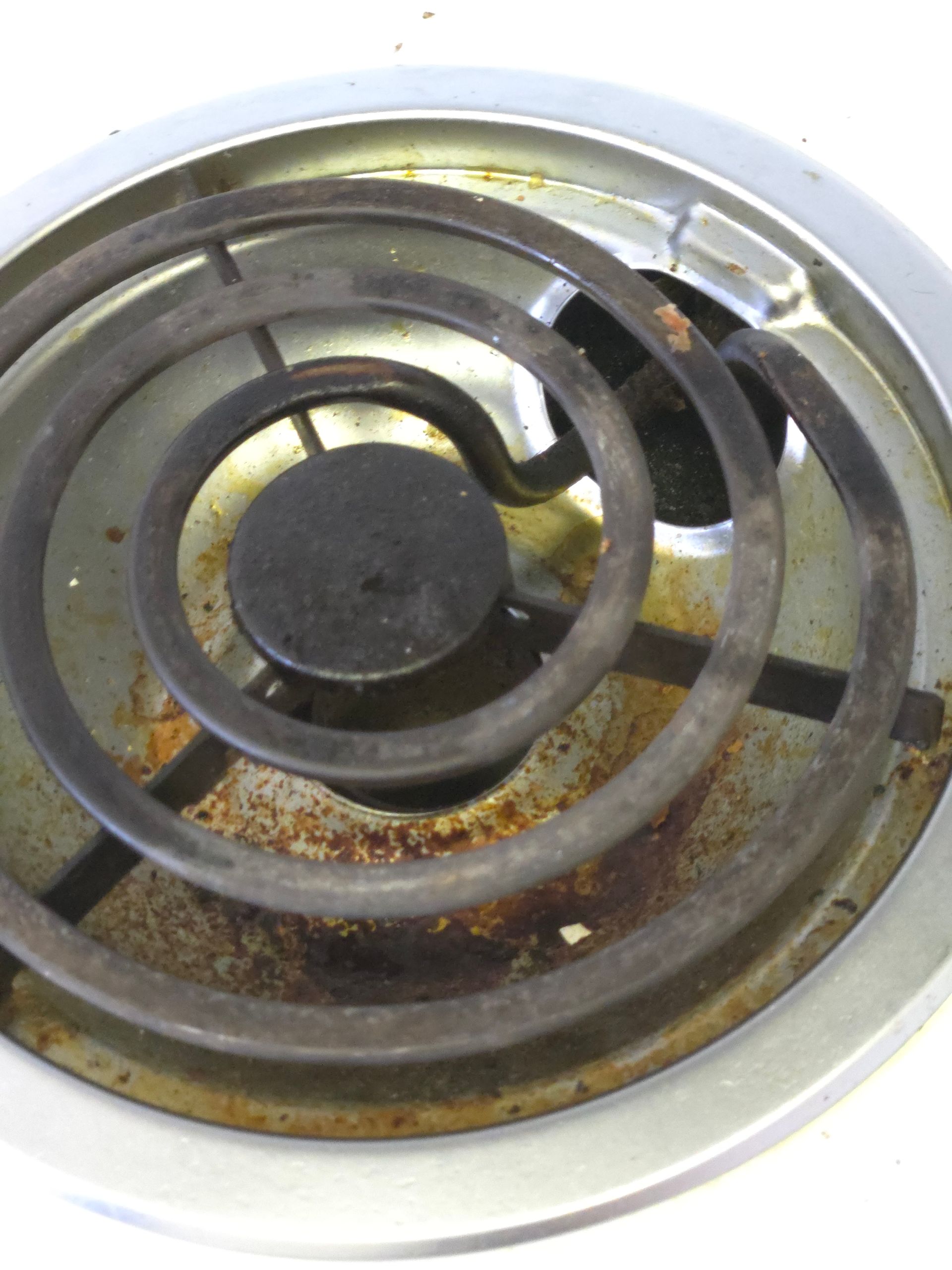 Close-up of a dirty, rusted electric stove burner coil and drip pan.