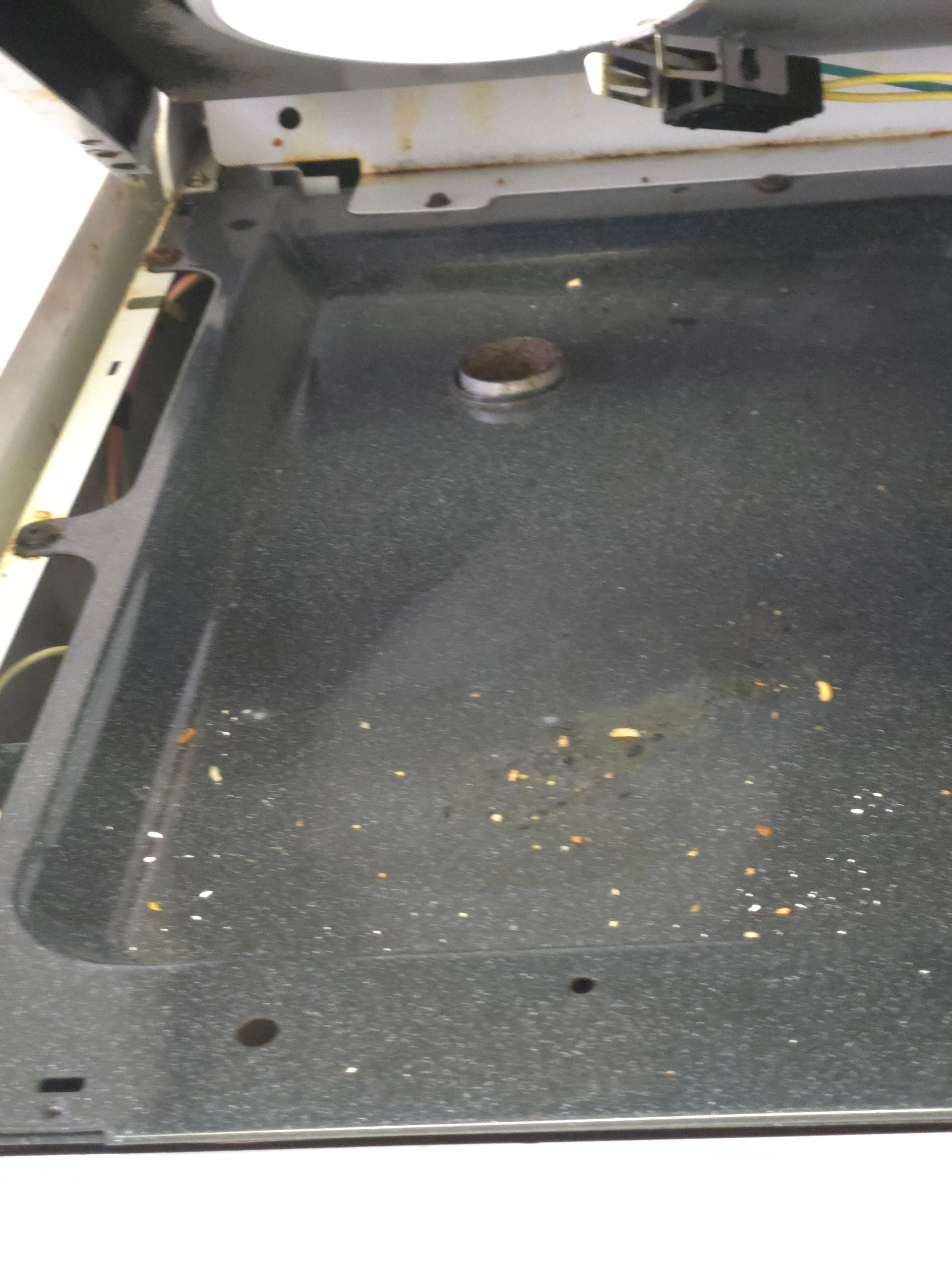 Black oven with a dirty, speckled bottom. There's a metal cylinder and small food debris scattered on the surface.