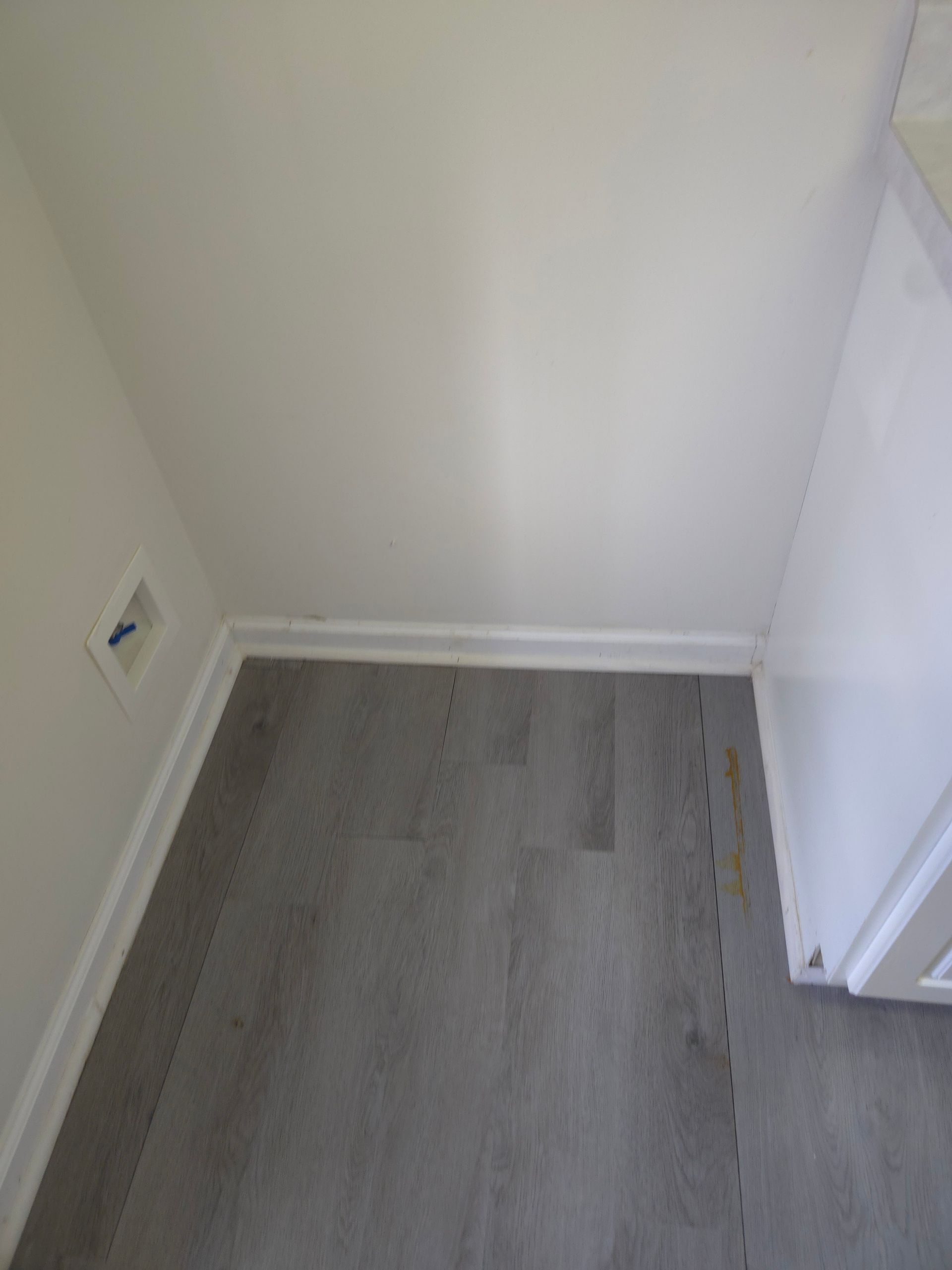 Corner of a room with gray flooring, white walls and trim. A white cabinet edge is on the right.