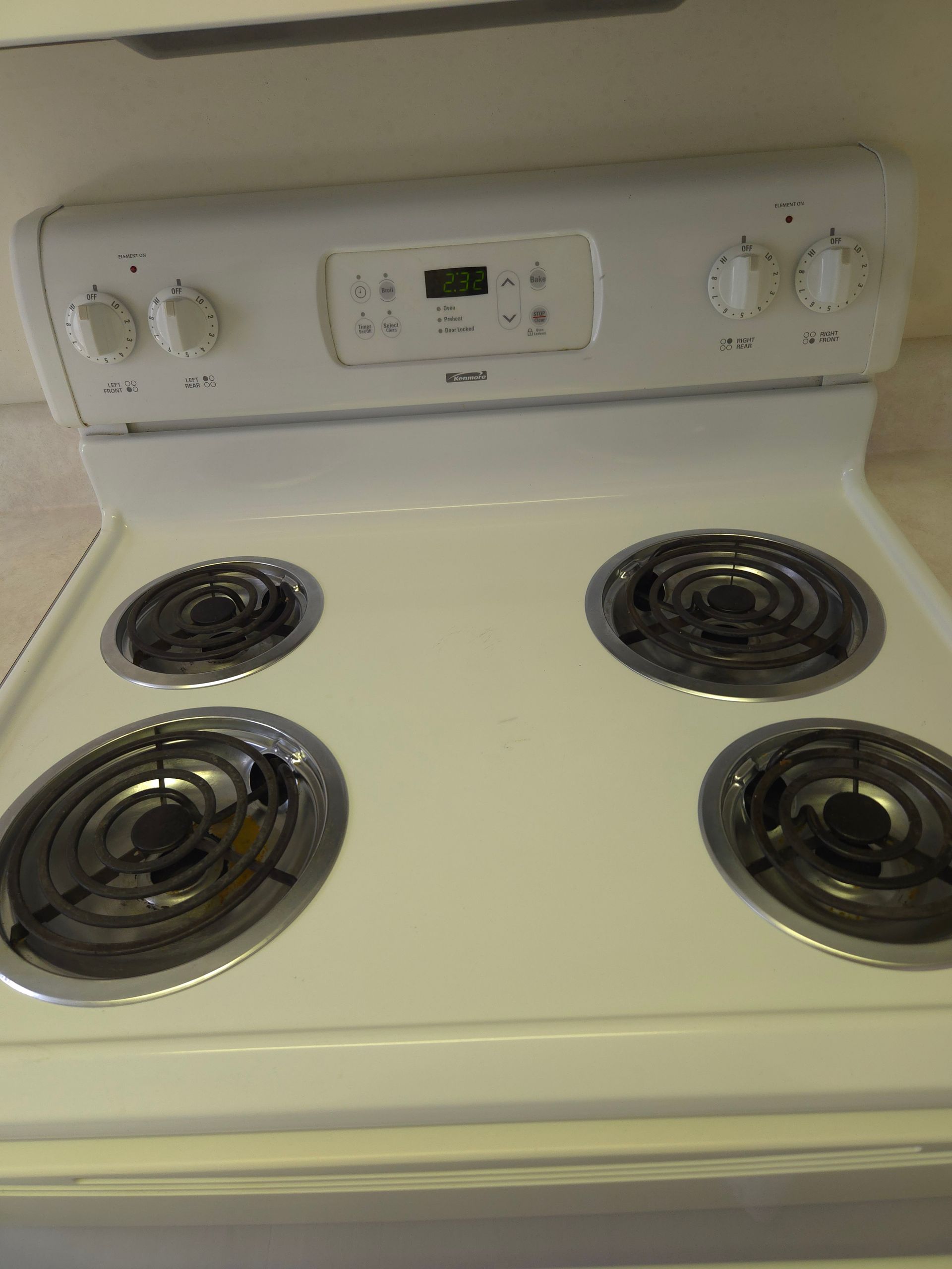 White electric stove with four burners and control panel with knobs and a digital display.