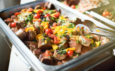 Tray of roasted potatoes, sausage, and vegetables topped with chopped herbs and cherry tomatoes