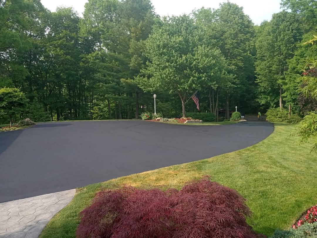 A black asphalt driveway surrounded by trees and grass.