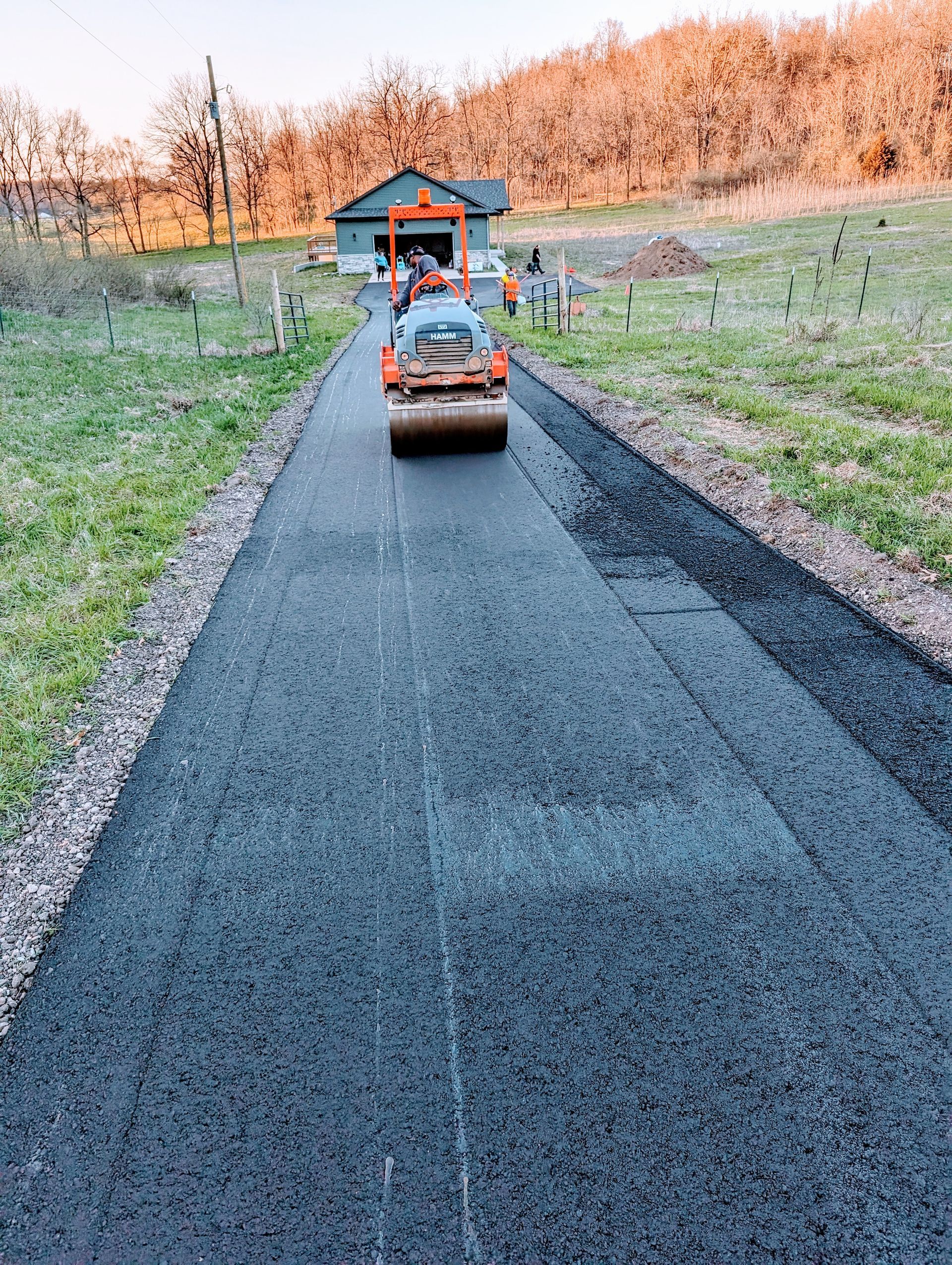 A roller is rolling asphalt on a road in front of a house.