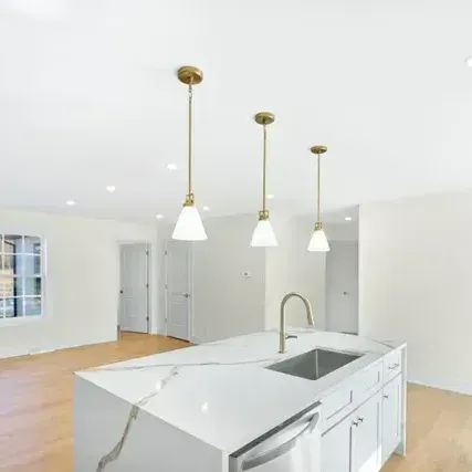 Kitchen island with pendant lights, sink, and faucet. Light wood floor, white walls and cabinets.