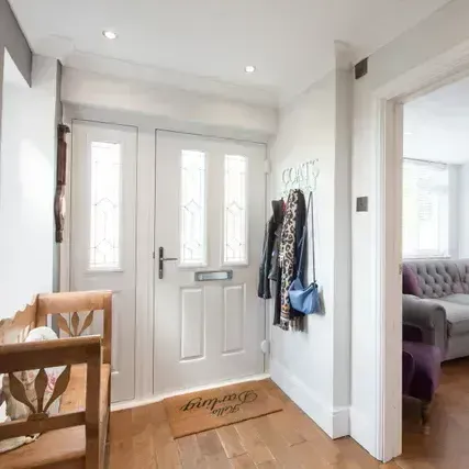 Entryway with white door, coat rack, wooden bench, and view into living room with a sofa.