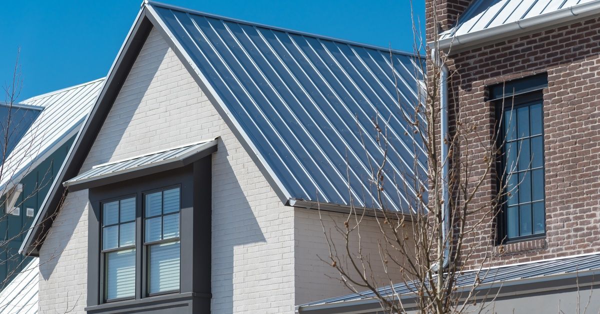 Silver metal roof panels run down the steep gables of a residential home. A leafless tree stands in