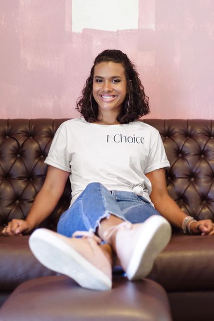 A woman is sitting on a couch wearing a t-shirt that says 1st choice