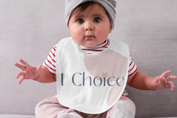 A baby wearing a bib that says i 'm choice is sitting on a couch.