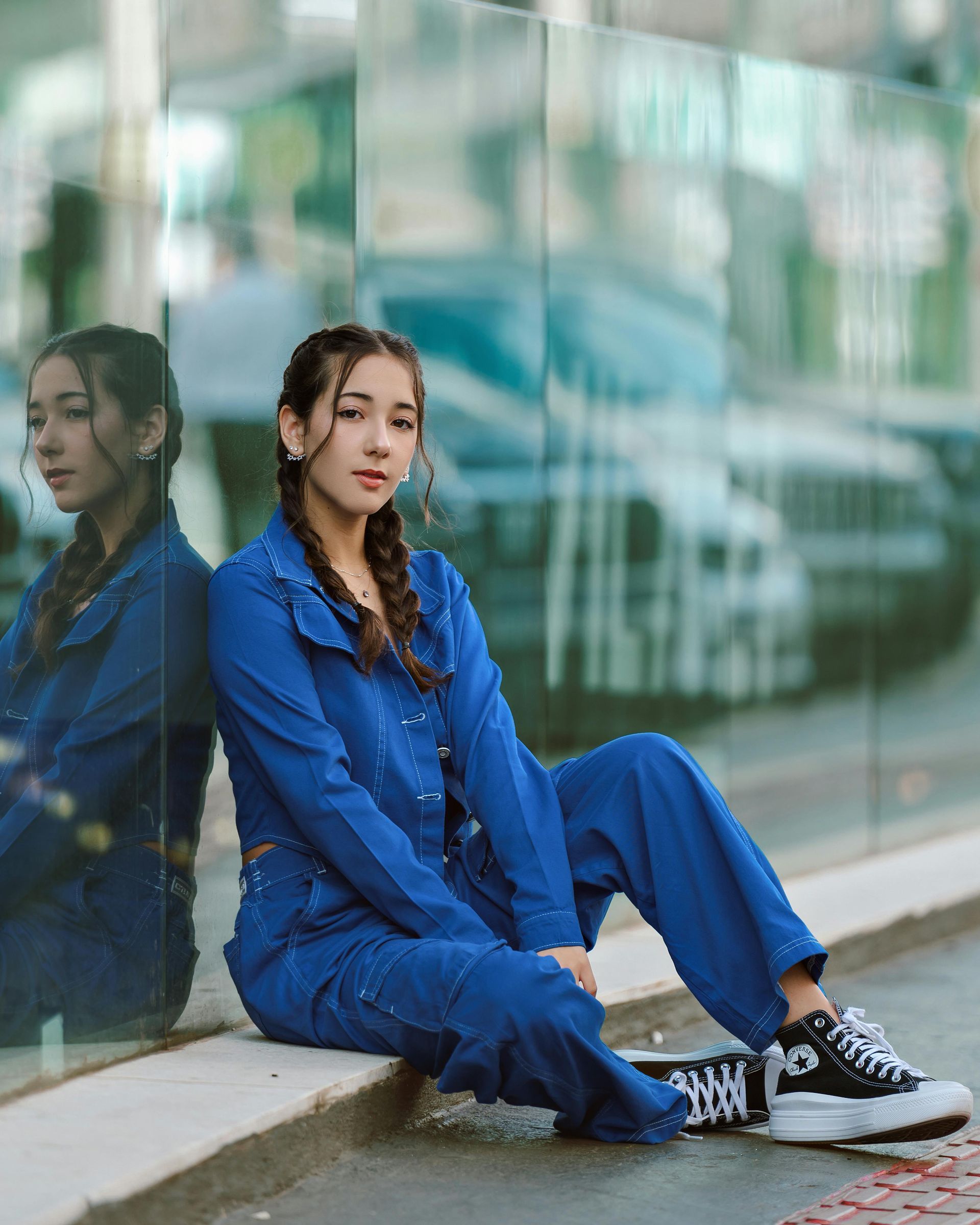 A woman in a blue jumpsuit is sitting on the sidewalk