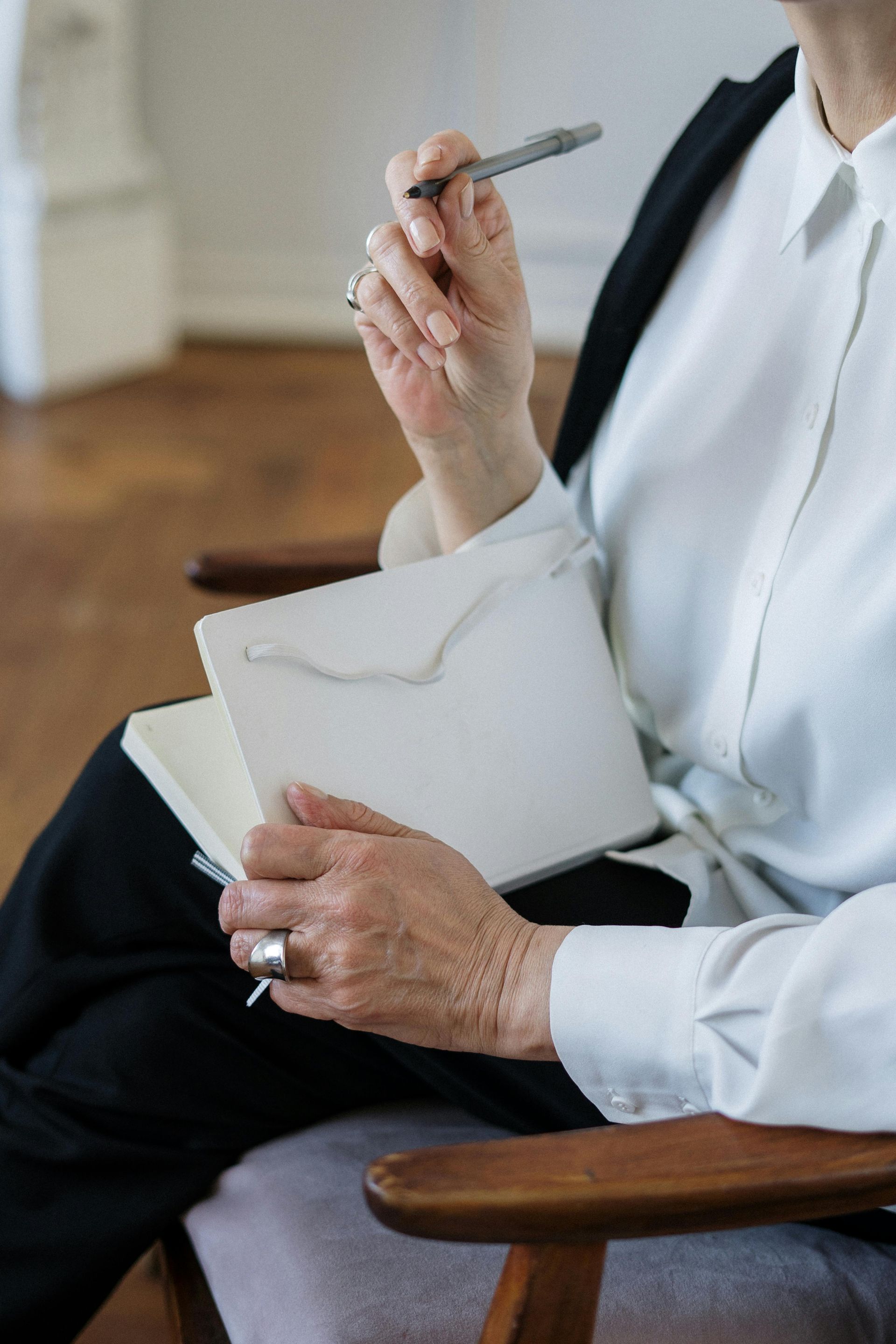 A woman is sitting in a chair holding a pen and a notebook.