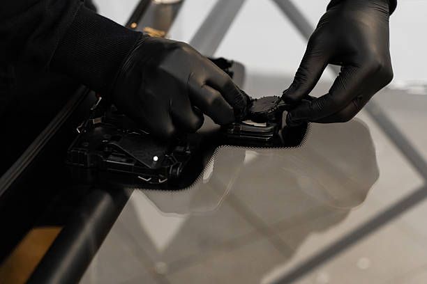 Close-up of gloved hands applying adhesive sealant to a car frame during a windshield replacement procedure.