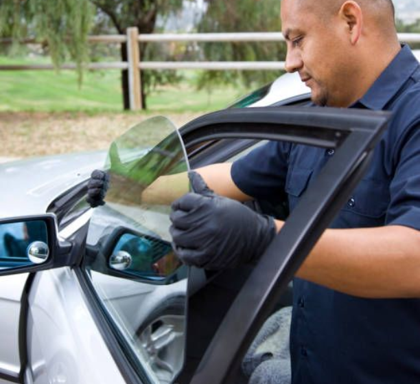 Auto glass repair specialist carefully installing a new driver side window into a car door.