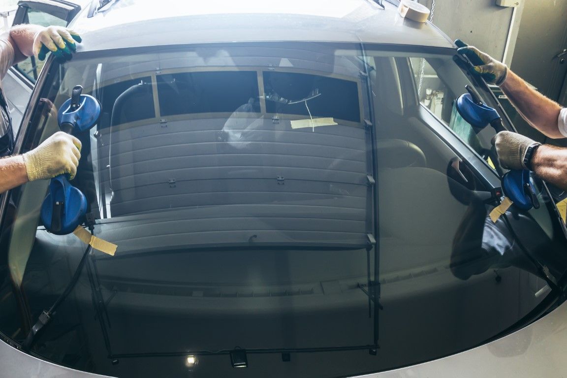 Car window repair mechanic fitting a new glass pane into the rear door panel of a sedan.