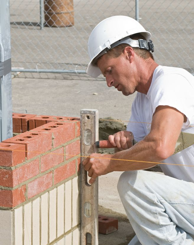 Construction worker using a level to build a brick wall outdoors.