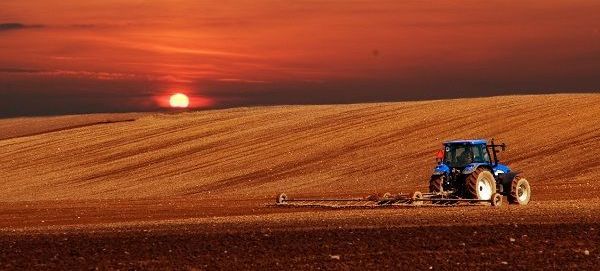 Um trator azul está arando um campo ao pôr do sol.