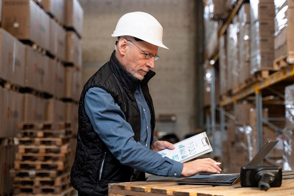 Um homem com capacete está usando um laptop em um armazém.