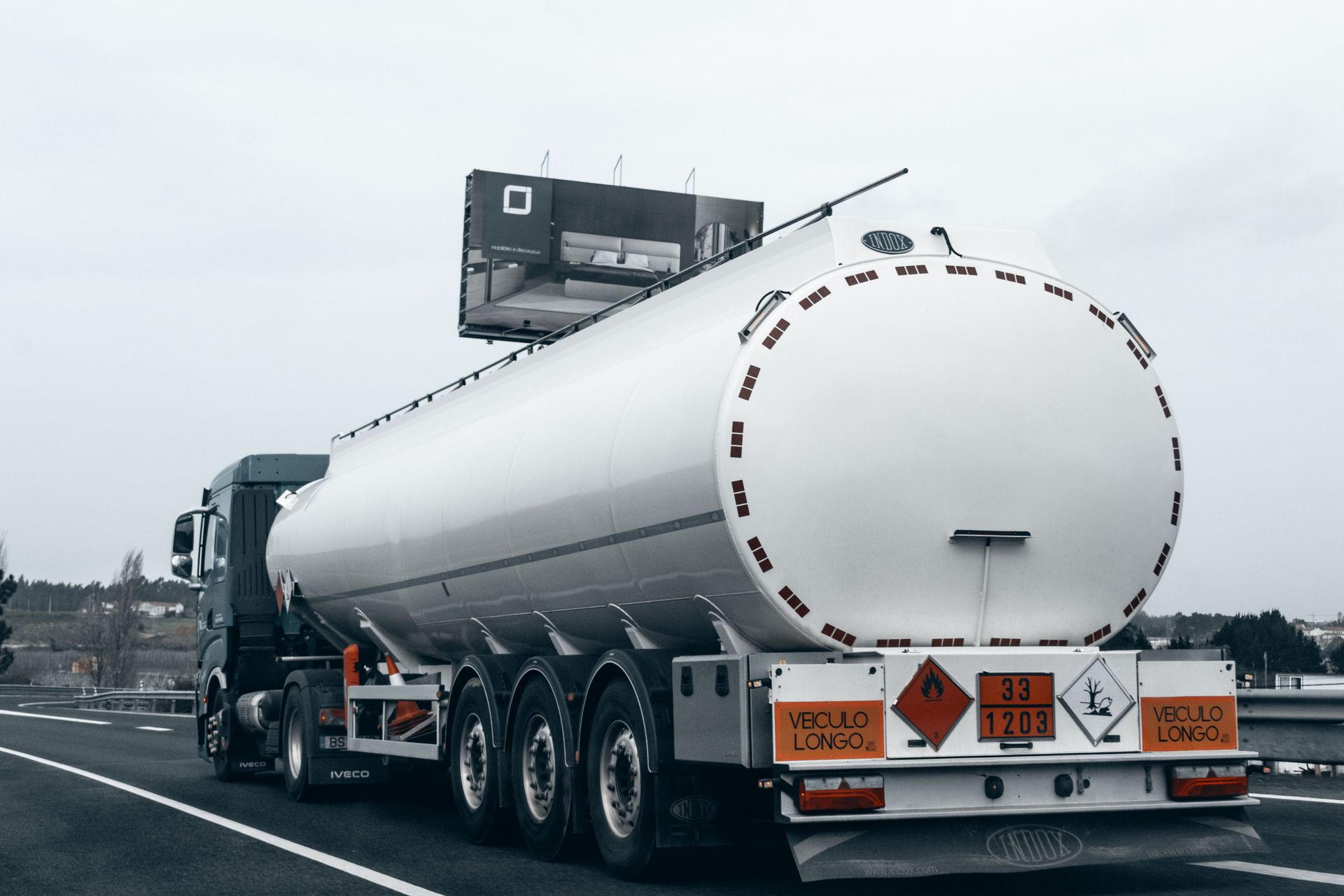 White tanker truck driving on a highway, rear view with reflective hazard signs