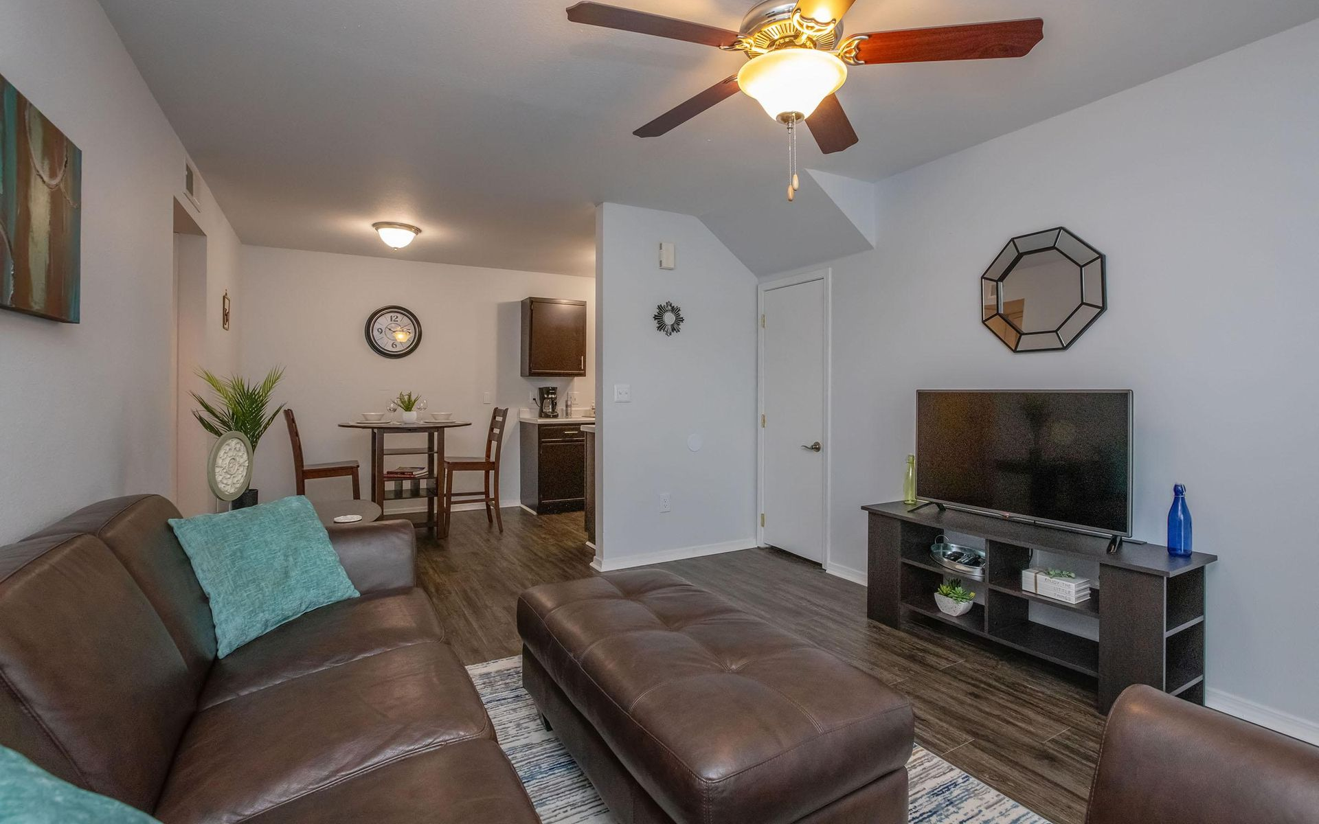Cozy living room with brown leather sofa, TV, ottoman, dining area, and ceiling fan.