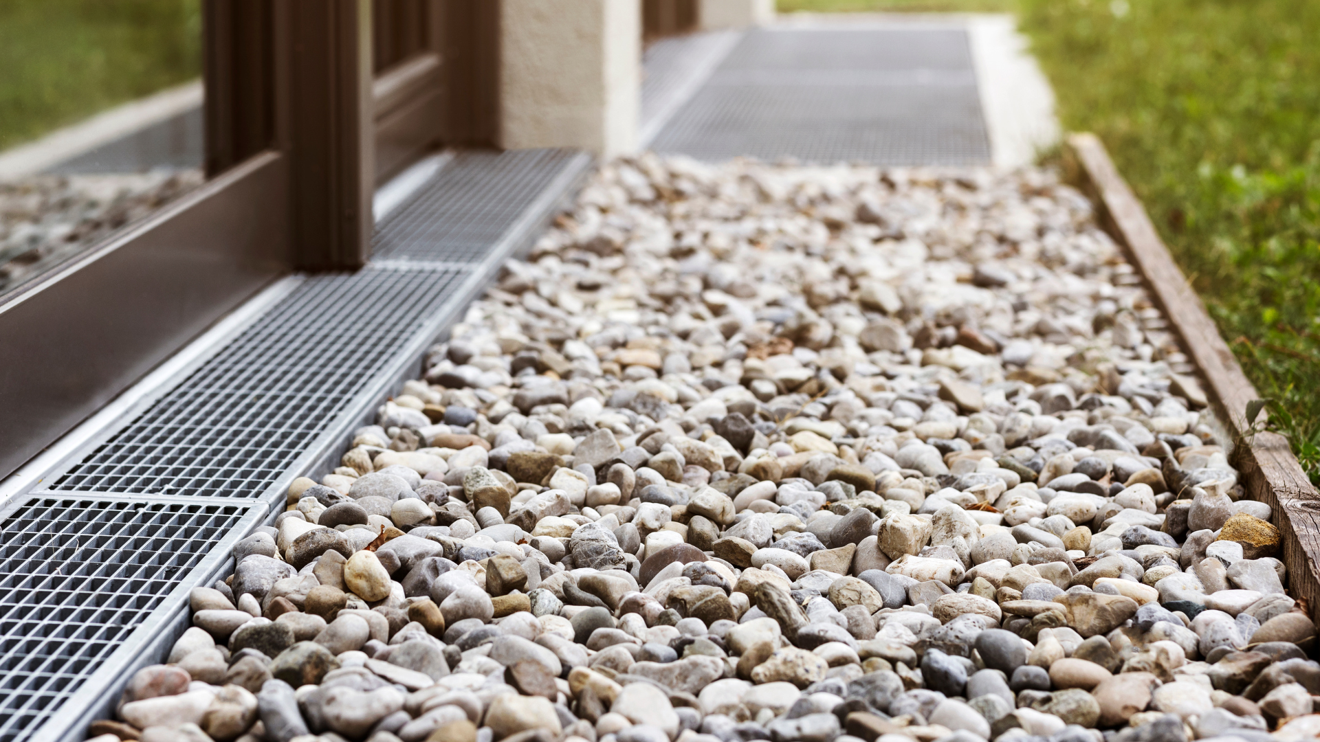 Gravel path next to a building with a metal grate drain, grass visible.
