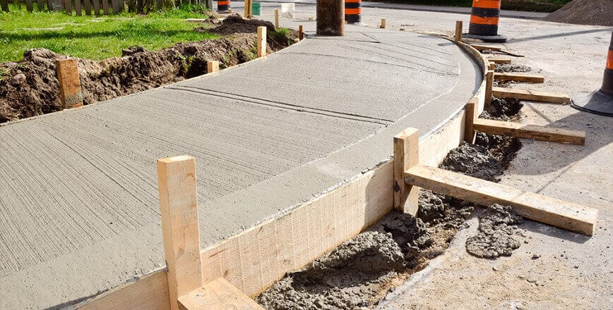 A concrete walkway is being built on the side of a road