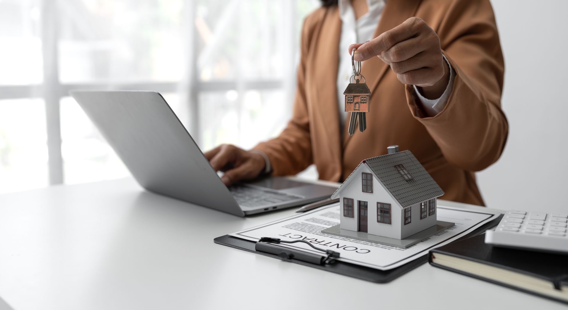 Real estate agent handing over house keys next to a model home during closing
