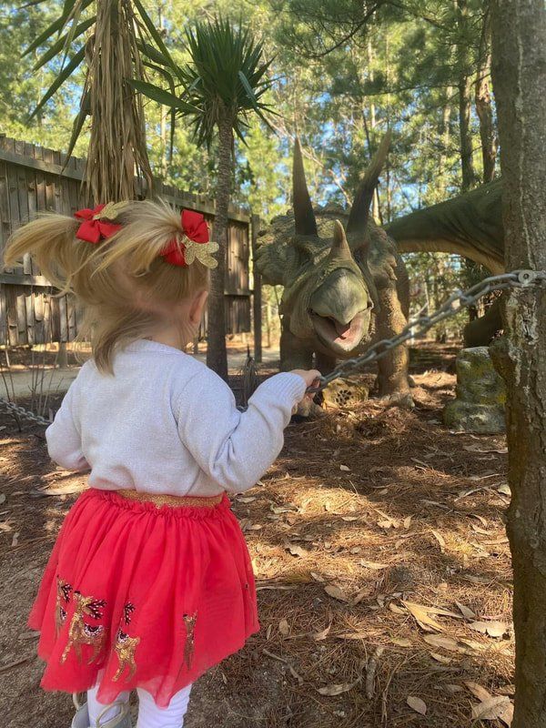 A little girl in a red skirt is standing in front of a dinosaur.