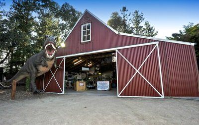 A t-rex statue is standing in front of a red barn