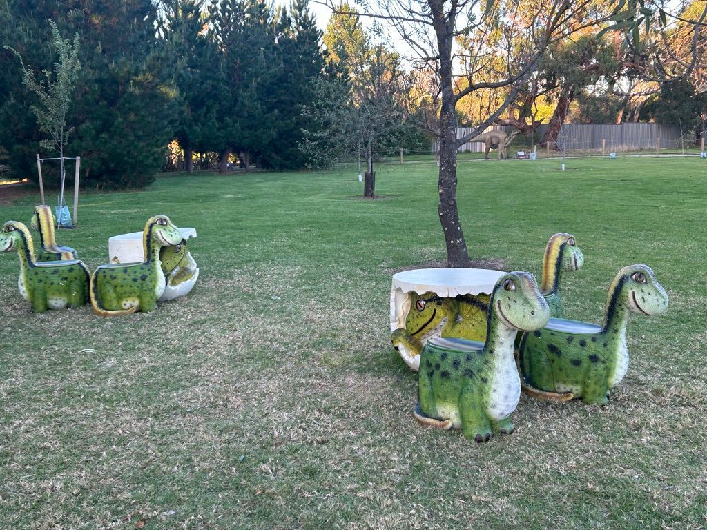 A group of dinosaur shaped chairs and tables in a park.