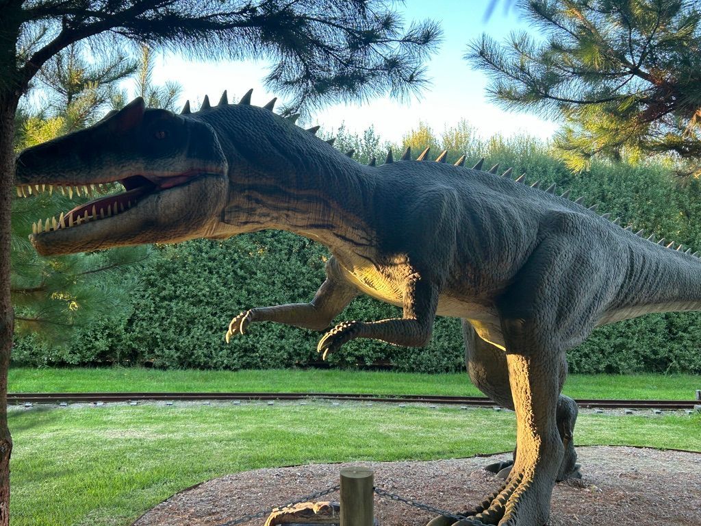 A statue of a dinosaur is standing next to a tree in a park.