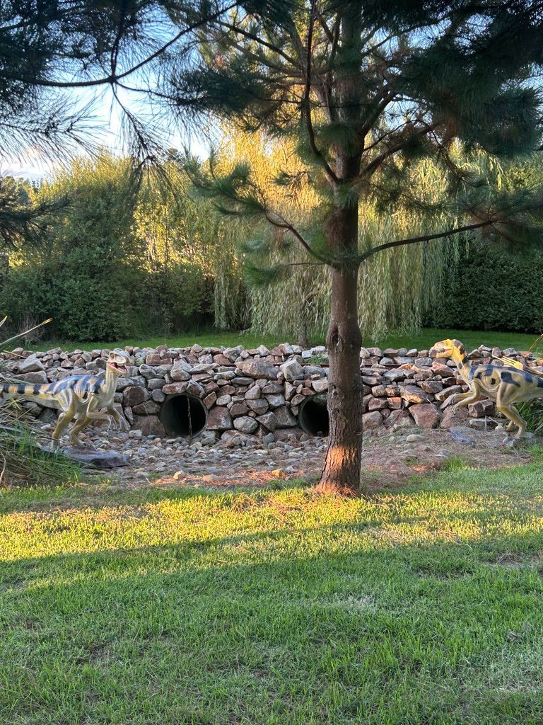 A group of dinosaurs standing next to a tree in a park.
