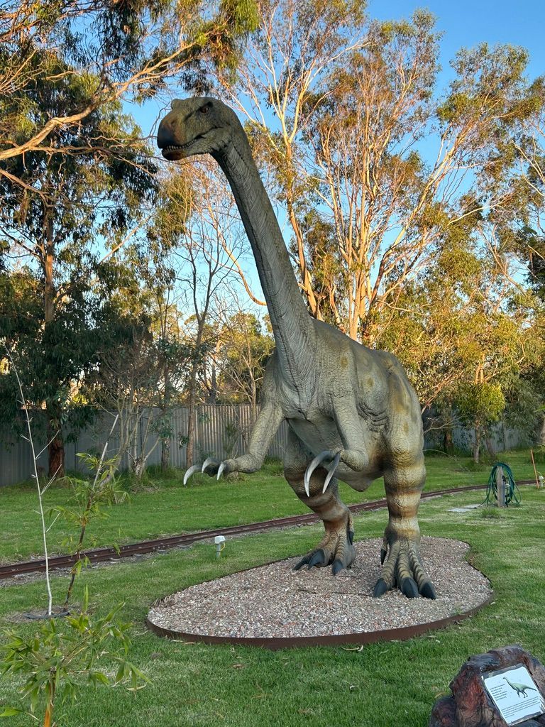A statue of a dinosaur is standing in the grass in a park.