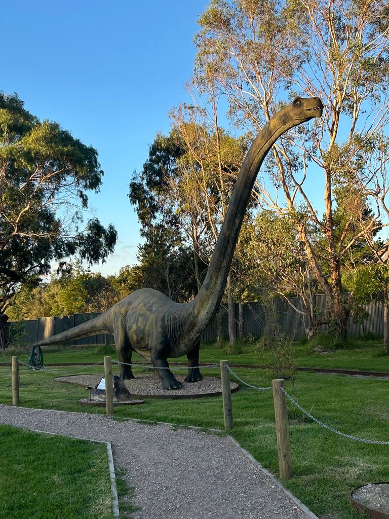 A statue of a dinosaur with a long neck is standing in a park.