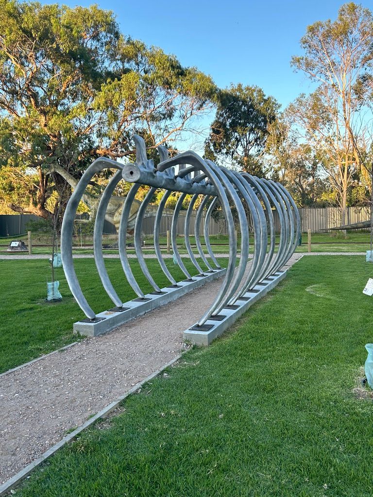 A large metal sculpture of a skeleton in a park.
