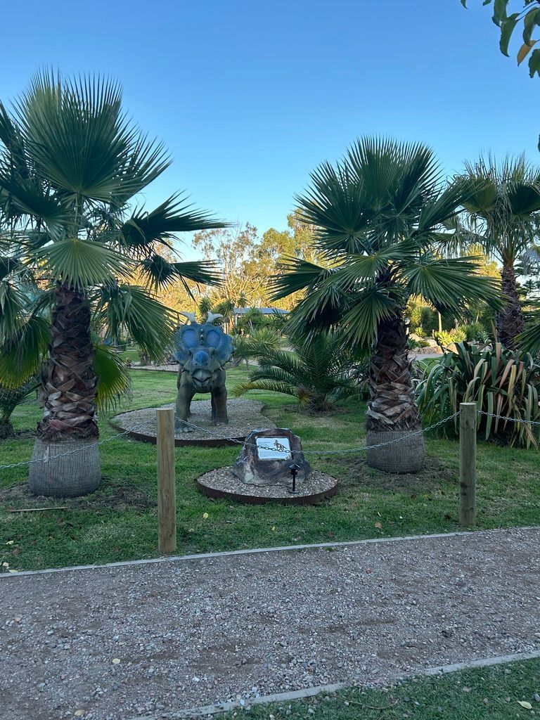 A park with a dinosaur and palm trees.