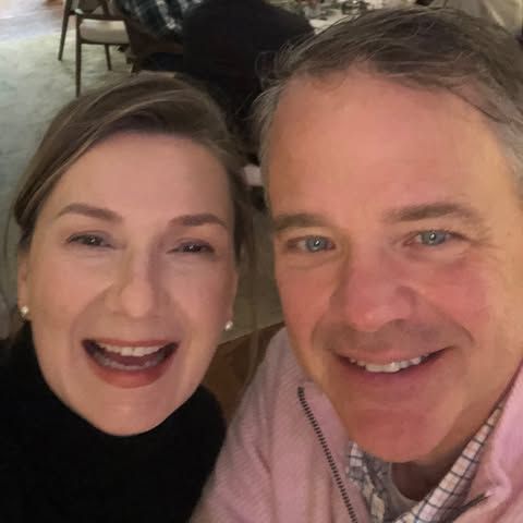 Woman with curly dark hair wearing round glasses smiles at the camera.