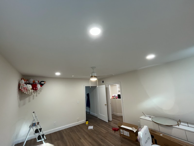 Empty room with recessed lighting and wood flooring; a doorway leads to another room.
