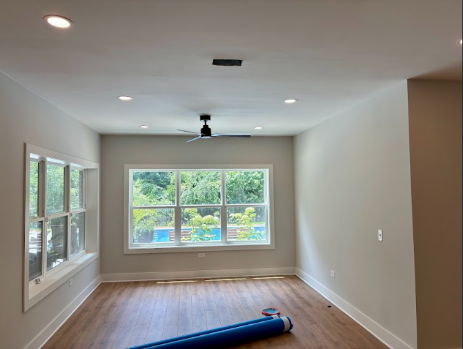 Empty room with windows, ceiling fan, and recessed lighting. Light wood flooring, neutral walls.