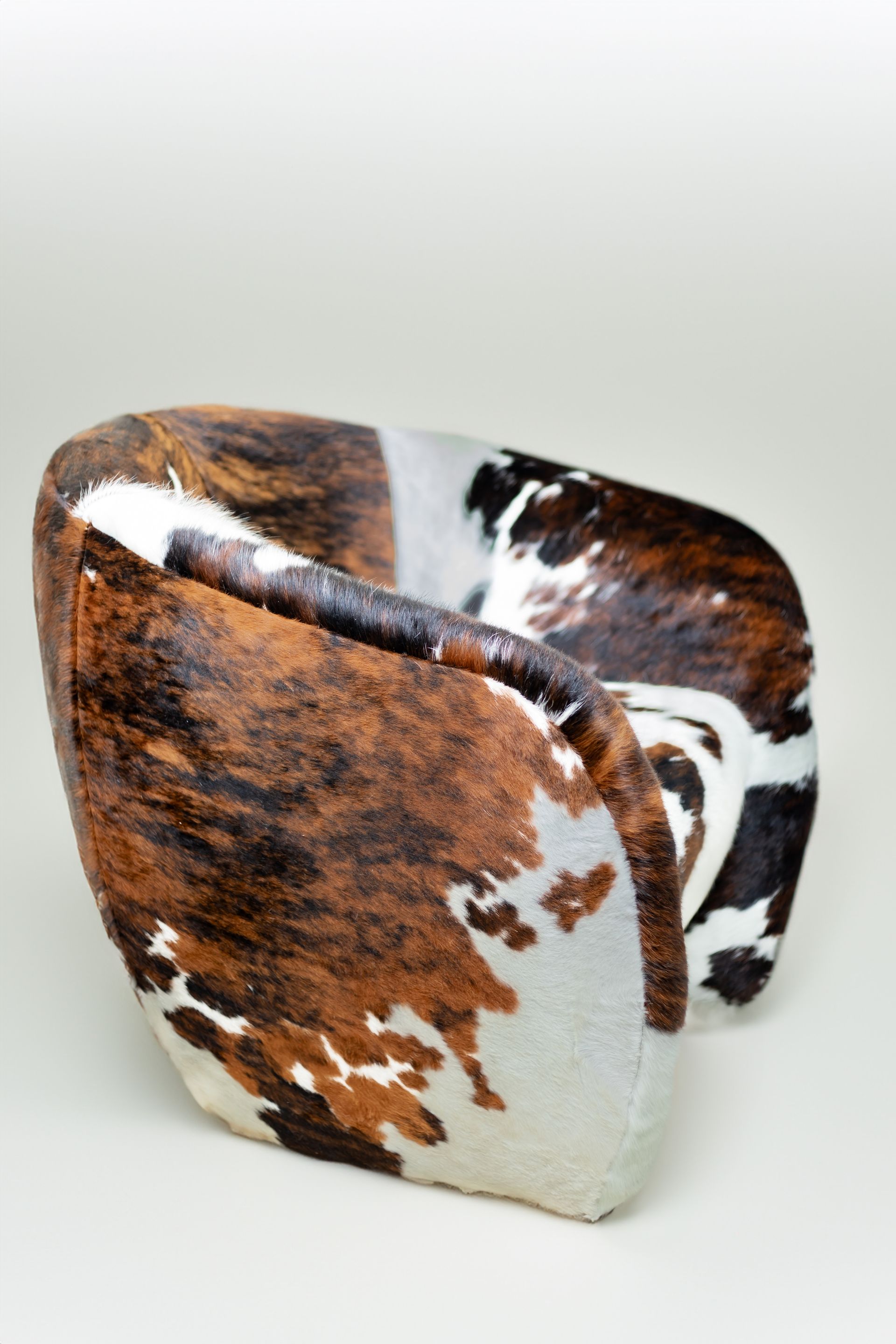 A brown and white cowhide chair is sitting on a white surface