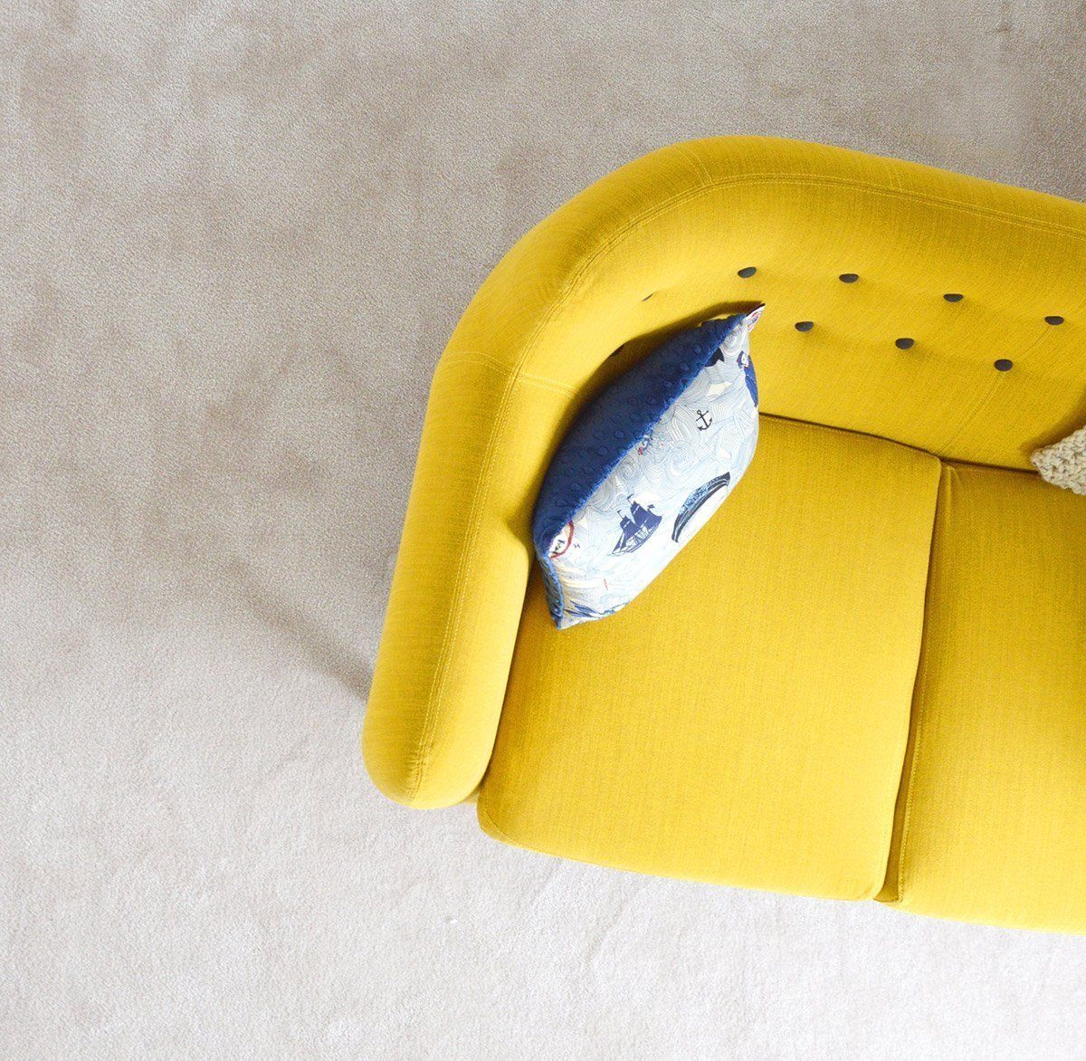 A yellow couch with a blue pillow on it